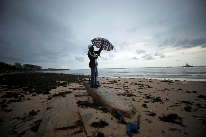 A man holds an umbrella beneath storm clouds over Wimbe beach in Pemba