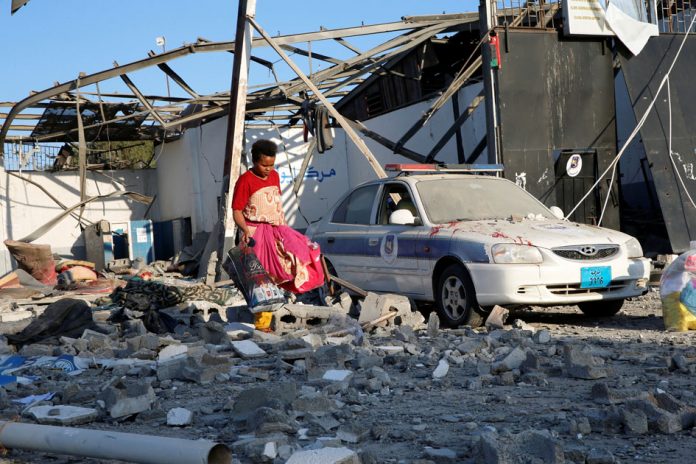 A migrant picks up clothes from among rubble at a detention centre for mainly African migrants that was hit by an airstrike in the Tajoura suburb of the Libyan capital of Tripoli