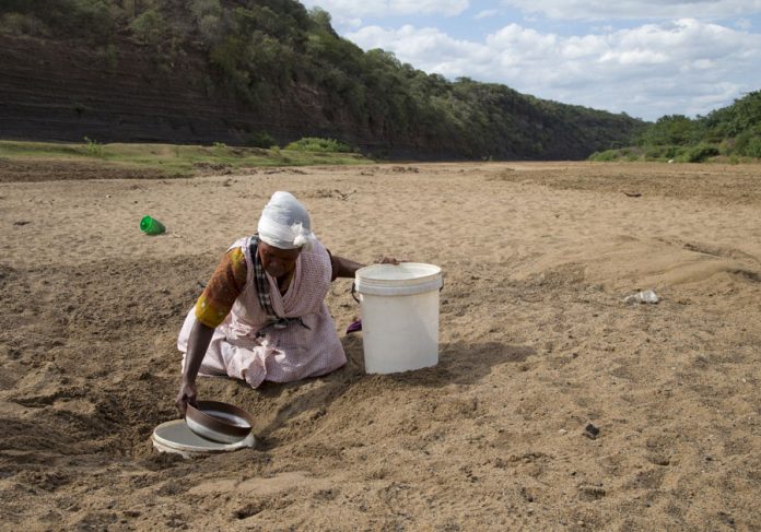 A woman gets water from a well dug in the Black Imfolozi River bed, which is dry due to drought, near Ulundi