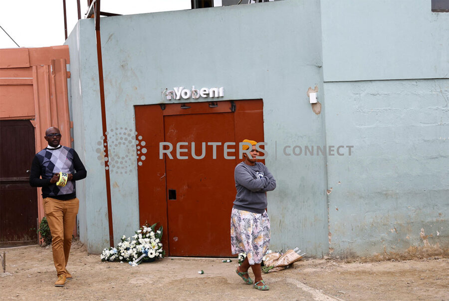 Vuyokazi Ndevu, the owner of Enyobeni tavern walks in front of a police officer ahead of a mass funeral in the Eastern Cape province, in East London