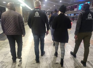 Wanted Ruth Lawrence with her blonde hair showing beneath her hat is escorted through Johannesburg Airport by two Interpol officers and one of the team of Irish detectives on the right carrying luggage heading for a waiting British Airways flight to Heathrow Airport.
