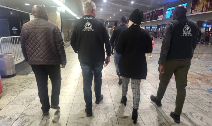 Ruth Lawrence extradited Wanted Ruth Lawrence with her blonde hair showing beneath her hat is escorted through Johannesburg Airport by two Interpol officers and one of the team of Irish detectives on the right carrying luggage heading for a waiting British Airways flight to Heathrow Airport.