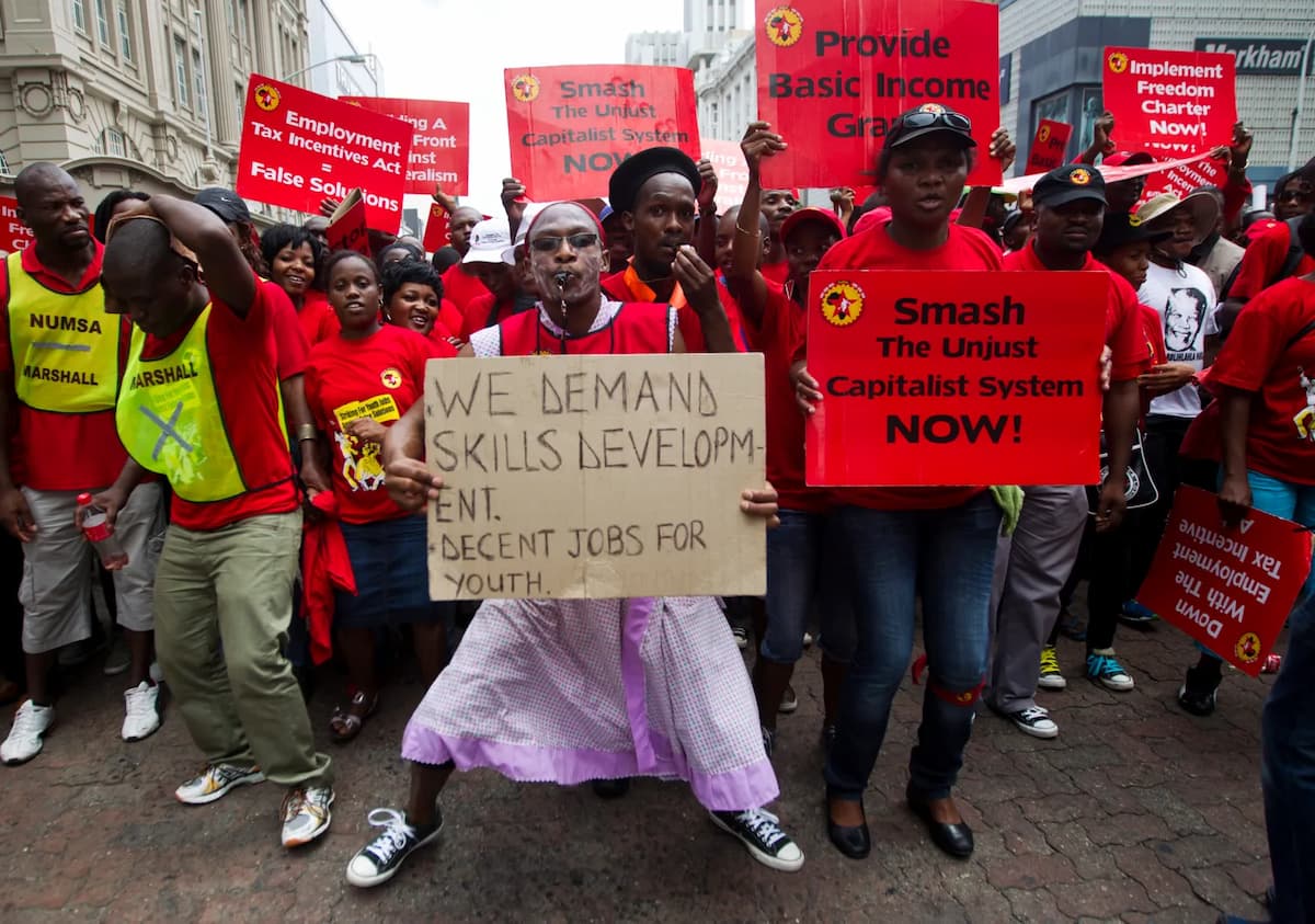 Picture depicts a protest related to South Africa jobs, with people holding placards. This image accompanies an article about unemployment and 'Who Is More Likely to Find Work – And Who Isn’t?'