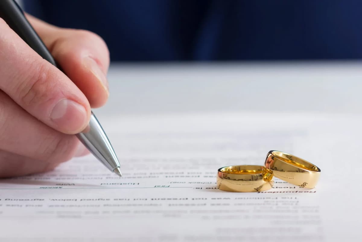 Stock image of wedding rings next to a hand signing a document. This image accompanies an article about women initiating divorce in South Africa in large numbers