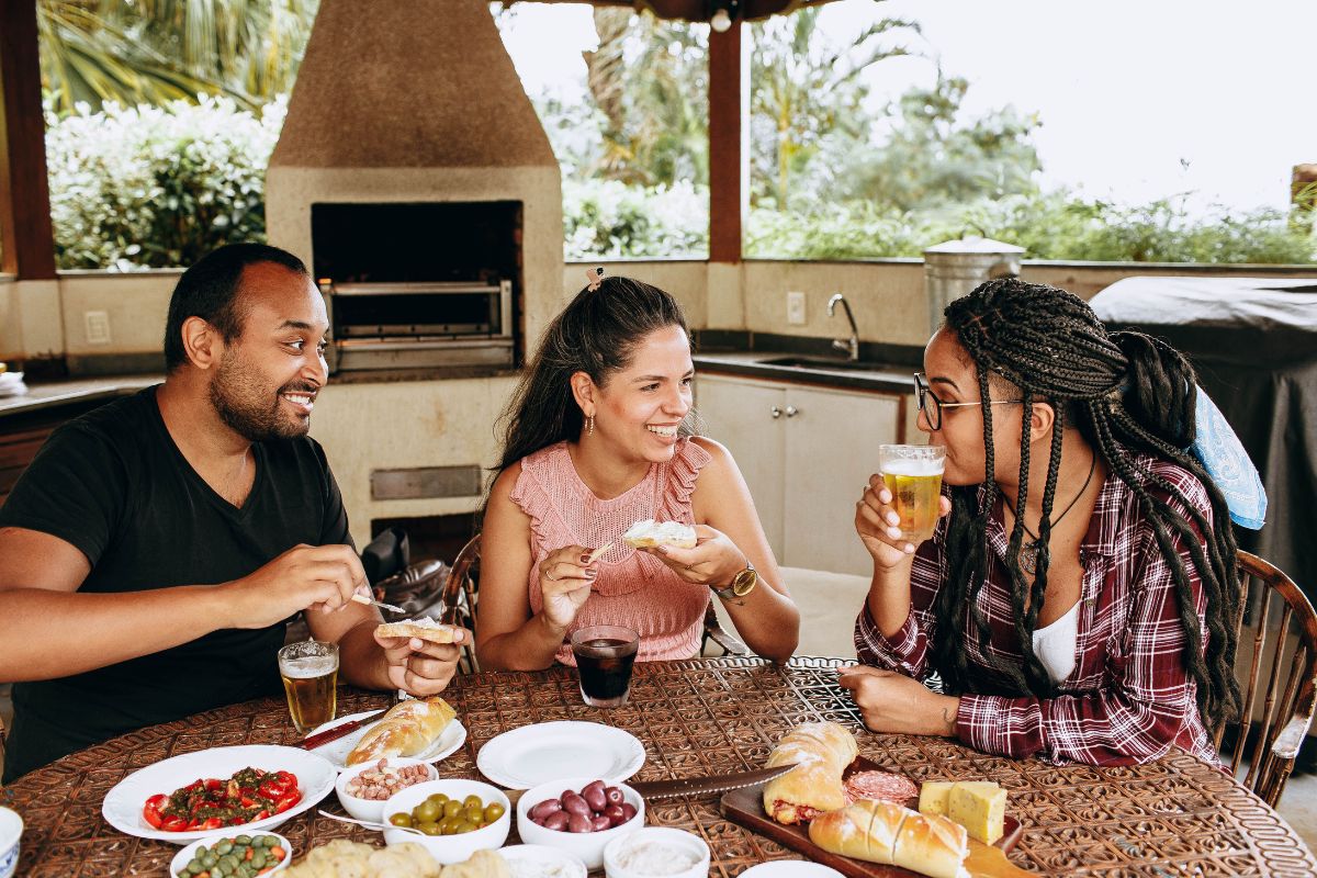 Three friends enjoying food and drinks together around a table, celebrating life's simple pleasures.